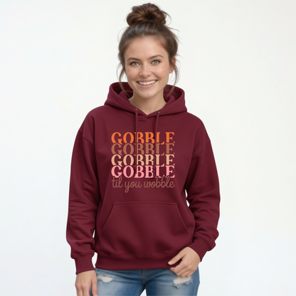 Woman modeling a maroon pullover hoodie featuring the colorful “Gobble Gobble Gobble Gobble til you wobble” Thanksgiving design with blue jeans.