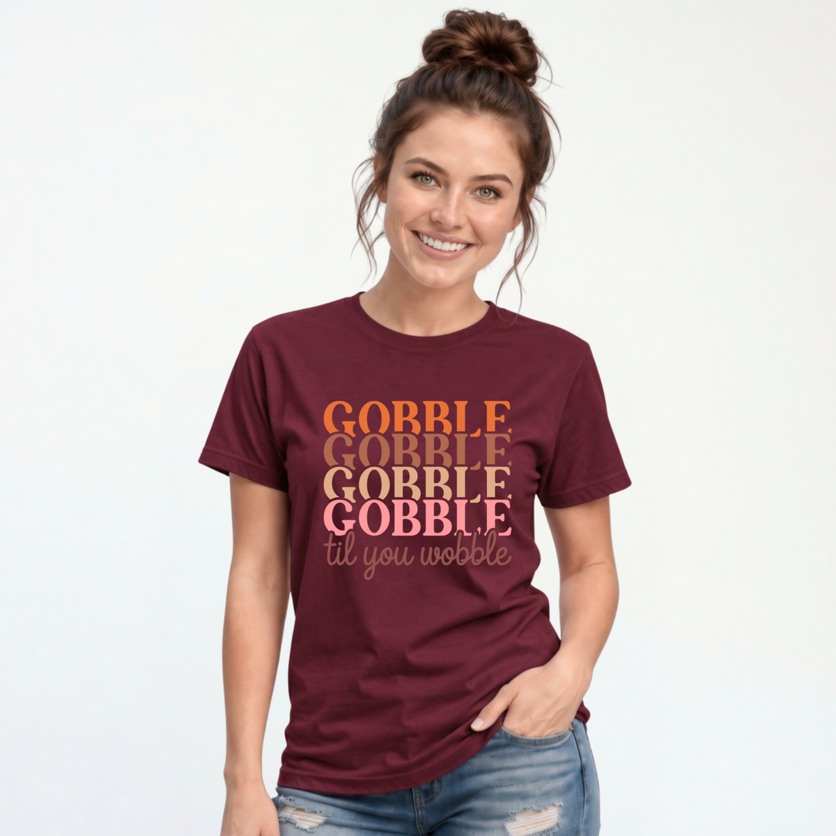 Woman wearing a maroon T-shirt with the “Gobble Gobble Gobble Gobble til you wobble” Thanksgiving design against a white studio background.