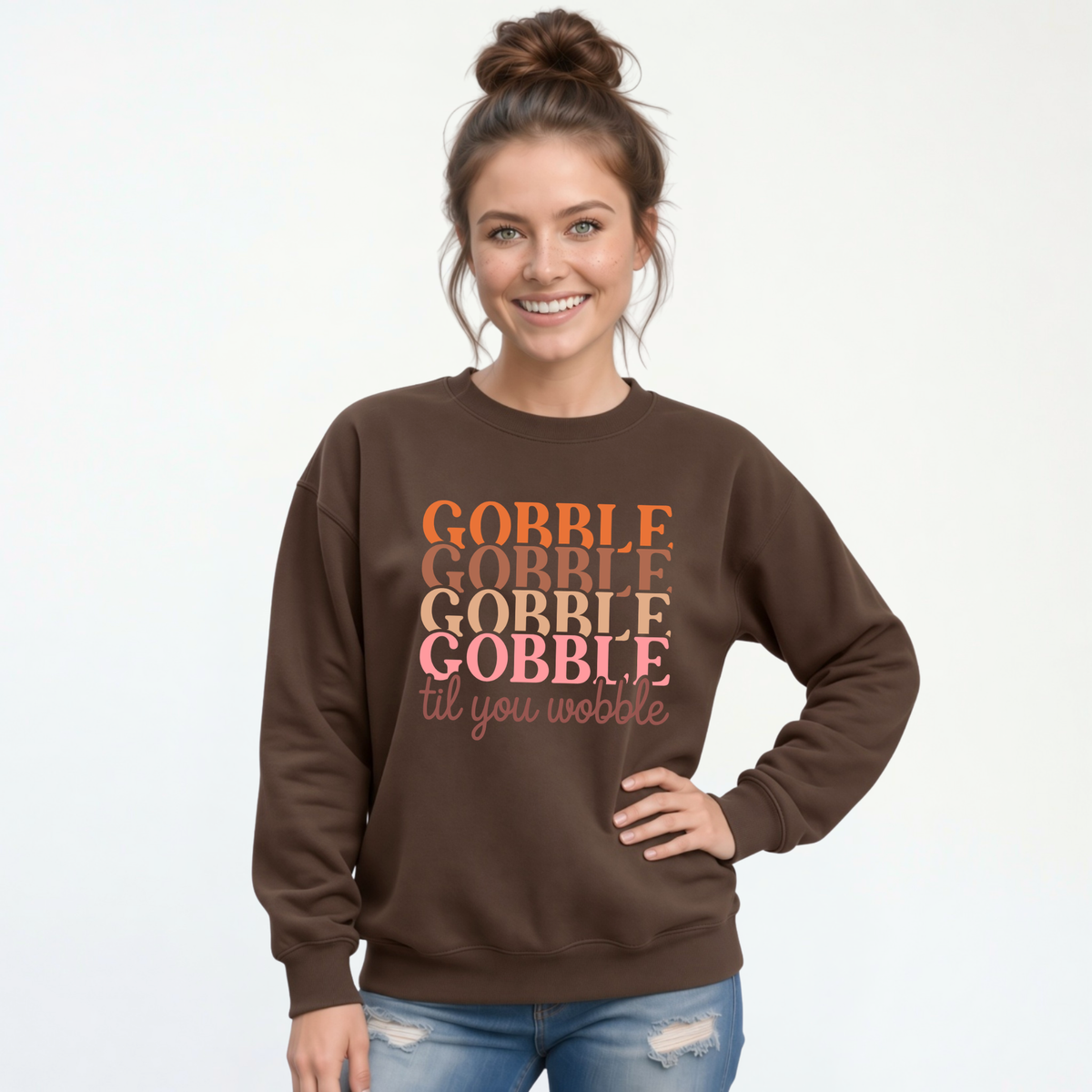 Woman modeling a brown crewneck sweatshirt with the stacked “Gobble Gobble Gobble Gobble til you wobble” design in warm fall colors.