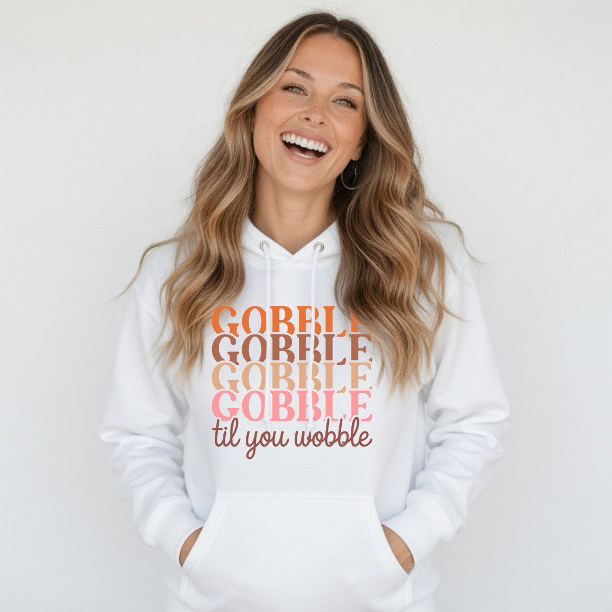 Smiling woman in a white pullover hoodie with the stacked “Gobble Gobble Gobble Gobble til you wobble” Thanksgiving design in warm fall colors.