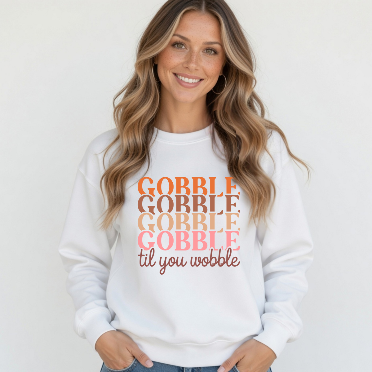 Blonde woman modeling a white crewneck sweatshirt with the colorful stacked “Gobble Gobble Gobble Gobble til you wobble” Thanksgiving design.