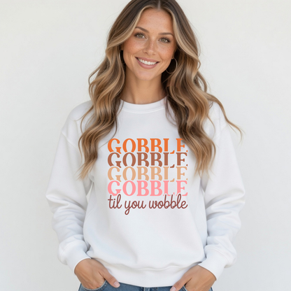 Blonde woman modeling a white crewneck sweatshirt with the colorful stacked “Gobble Gobble Gobble Gobble til you wobble” Thanksgiving design.