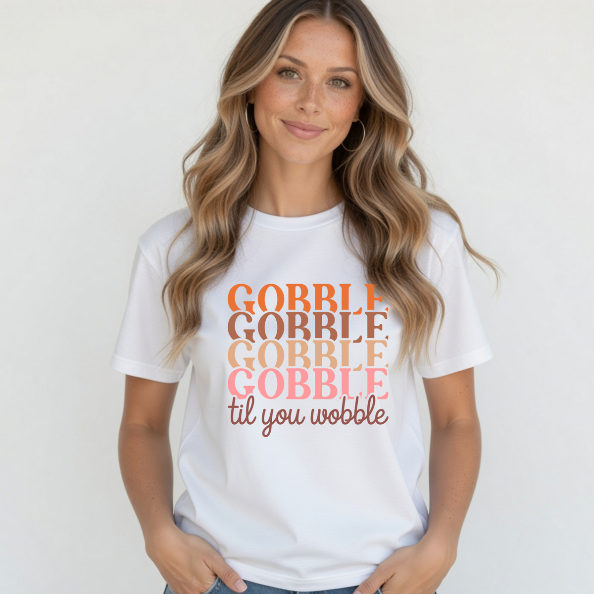 Blonde woman wearing a white T-shirt with the “Gobble Gobble Gobble Gobble til you wobble” Thanksgiving design against a white studio background.