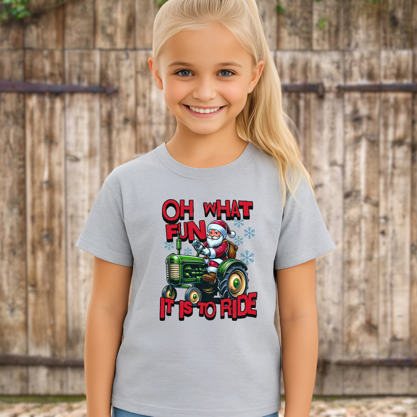 Smiling girl wearing a gray unisex Christmas shirt with Santa riding a tractor and the holiday phrase “Oh What Fun It Is to Ride