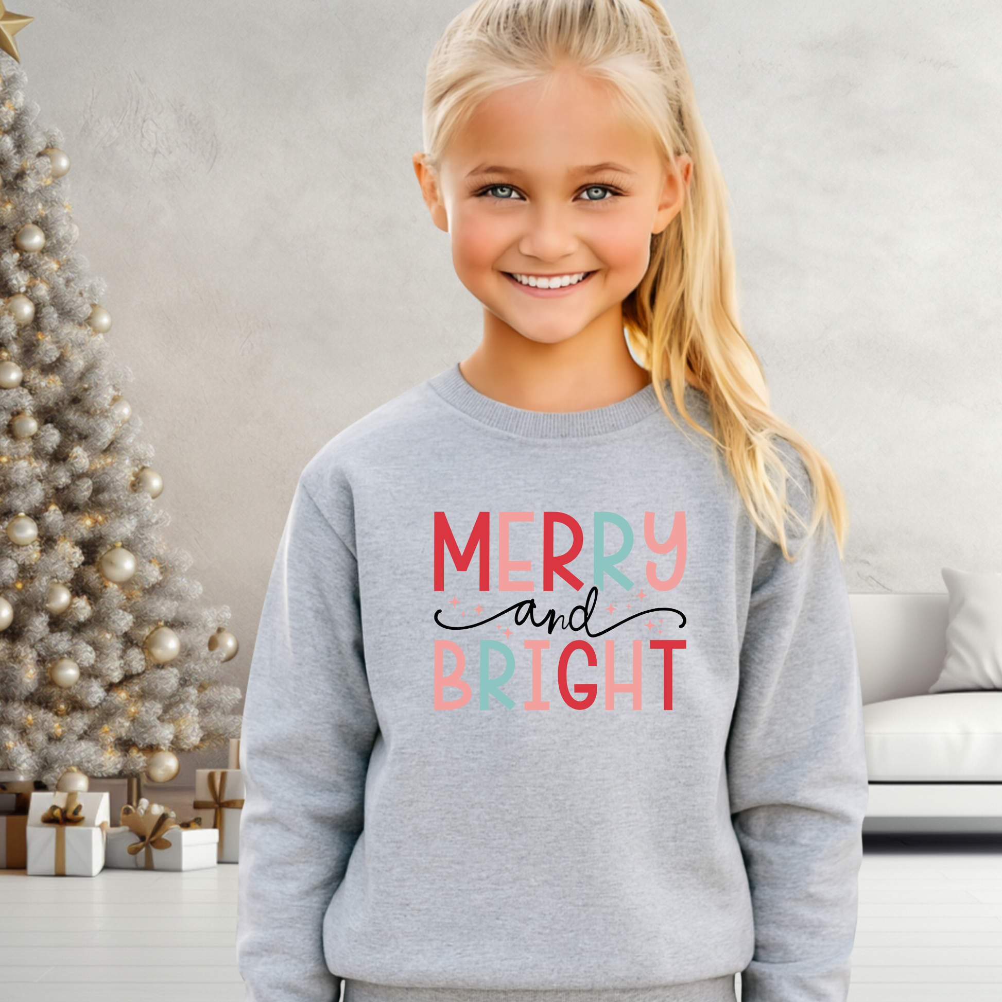 Young girl wearing a gray sweatshirt with 'Merry and Bright' text, standing in a room with a decorated Christmas tree.