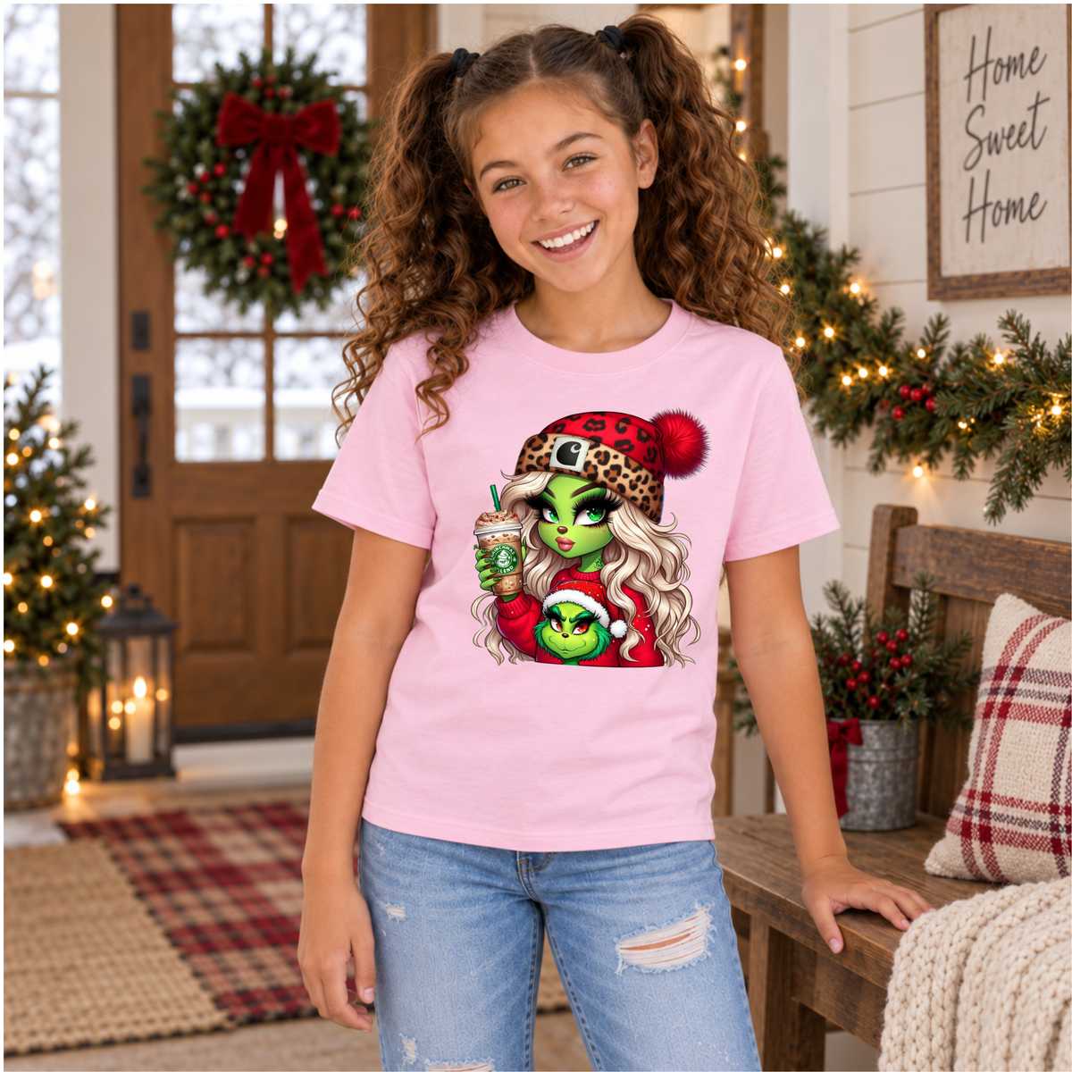 Youth light pink T-shirt with Boujee Green Girl Christmas graphic, modeled in a holiday decorated entryway