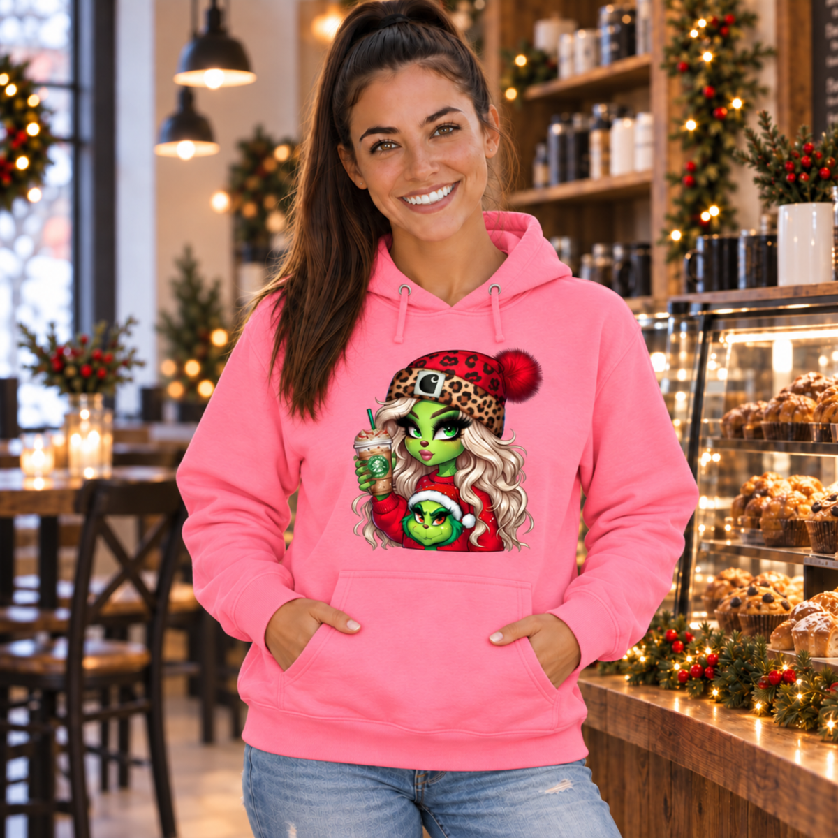 Woman wearing a pink hoodie with the Boujee Green Girl Christmas design in a holiday-decorated coffee shop