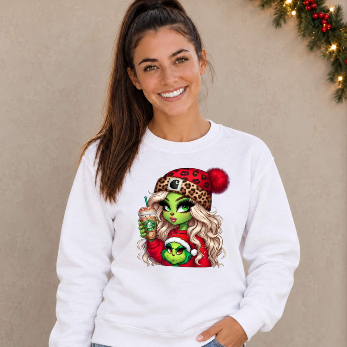 Woman wearing a white sweatshirt with a Boujee Green Girl Christmas design against a neutral wall with festive garland
