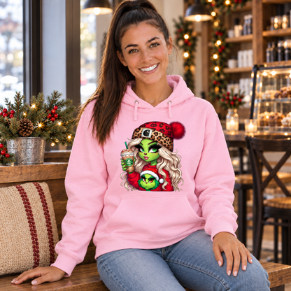 Woman seated in a holiday cafe wearing a light pink hoodie with the Boujee Green Girl Christmas design