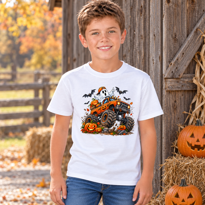 Boy modeling a white youth T-shirt featuring an orange Halloween monster truck with a ghost, pumpkins, and bats beside hay bales and carved jack-o-lanterns.