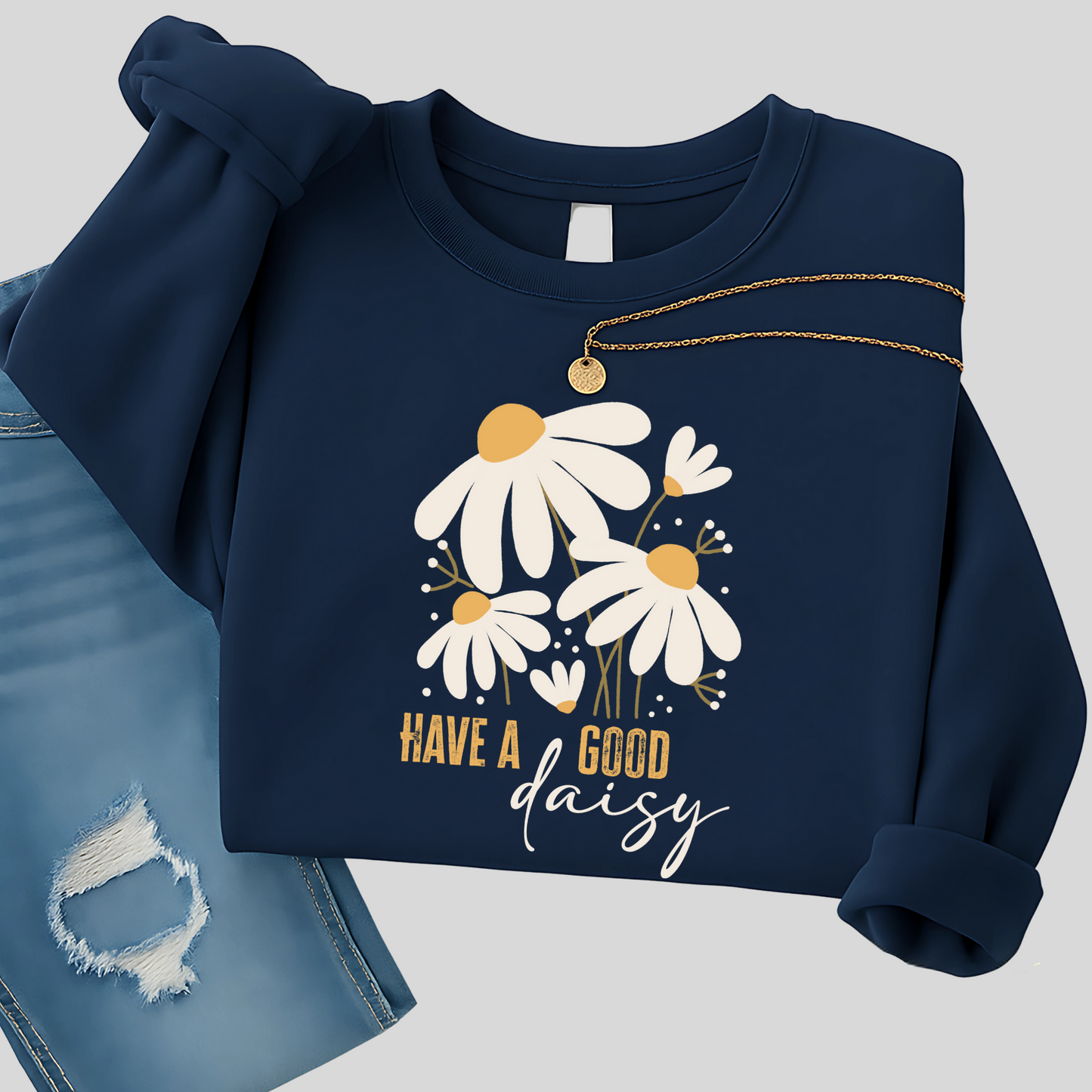 Navy blue floral sweatshirt with daisy graphic folded with distressed jeans and necklace, styled for cool fall days—great for casual outings, coffee runs, and relaxed fall fashion.