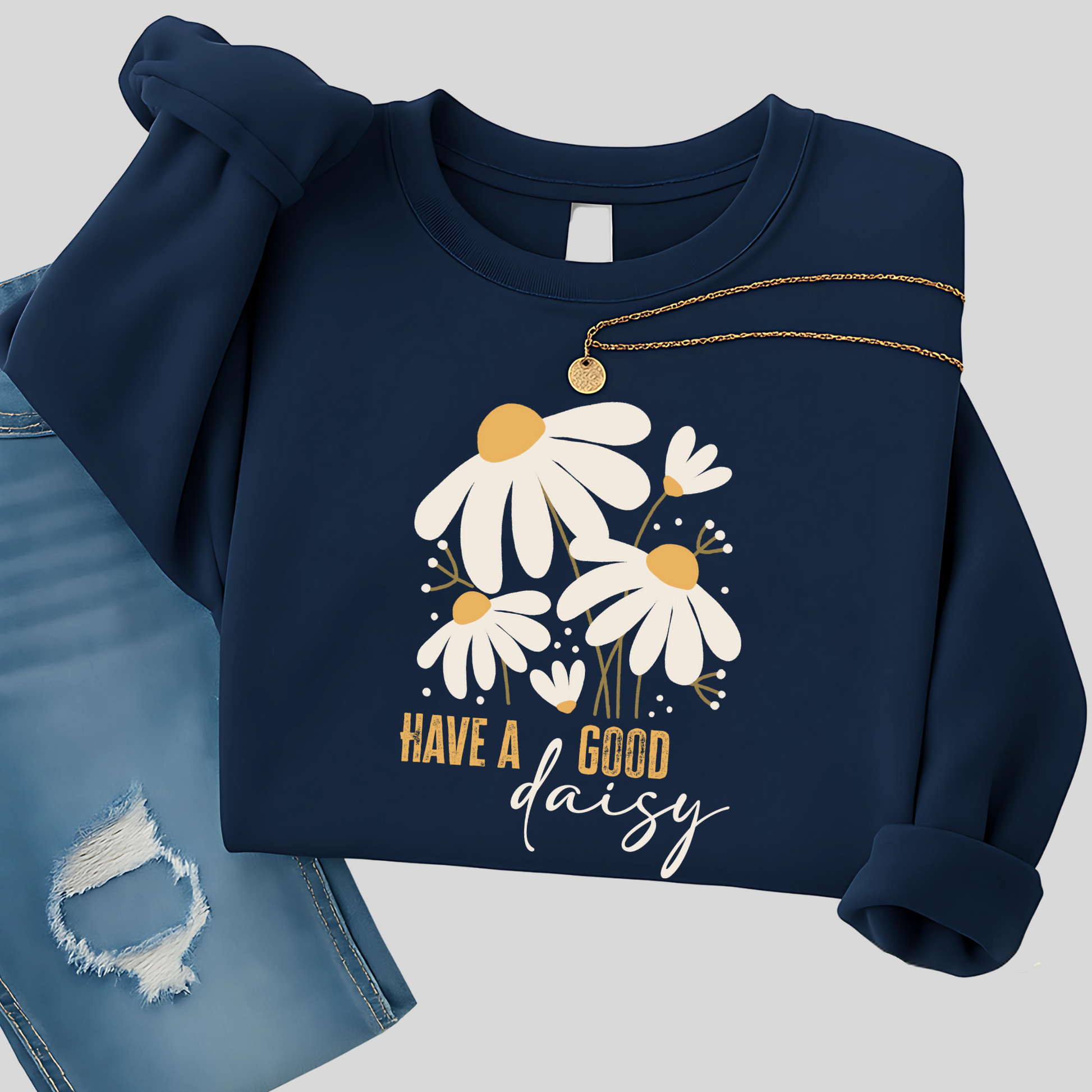 Navy blue floral sweatshirt with daisy graphic folded with distressed jeans and necklace, styled for cool fall days—great for casual outings, coffee runs, and relaxed fall fashion.