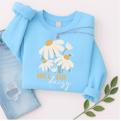 Sky blue floral sweatshirt with “Have a Good Daisy” design, laid out with jeans and greenery for a light, playful fall flat lay—perfect for transitional weather and cheerful cozy vibes.