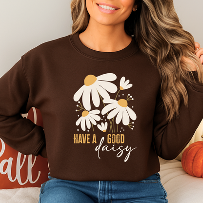 Smiling woman in a brown “Have a Good Daisy” sweatshirt with pumpkins and fall pillows, styled for the season—ideal for autumn photos, cozy gatherings, or a cute Thanksgiving outfit.