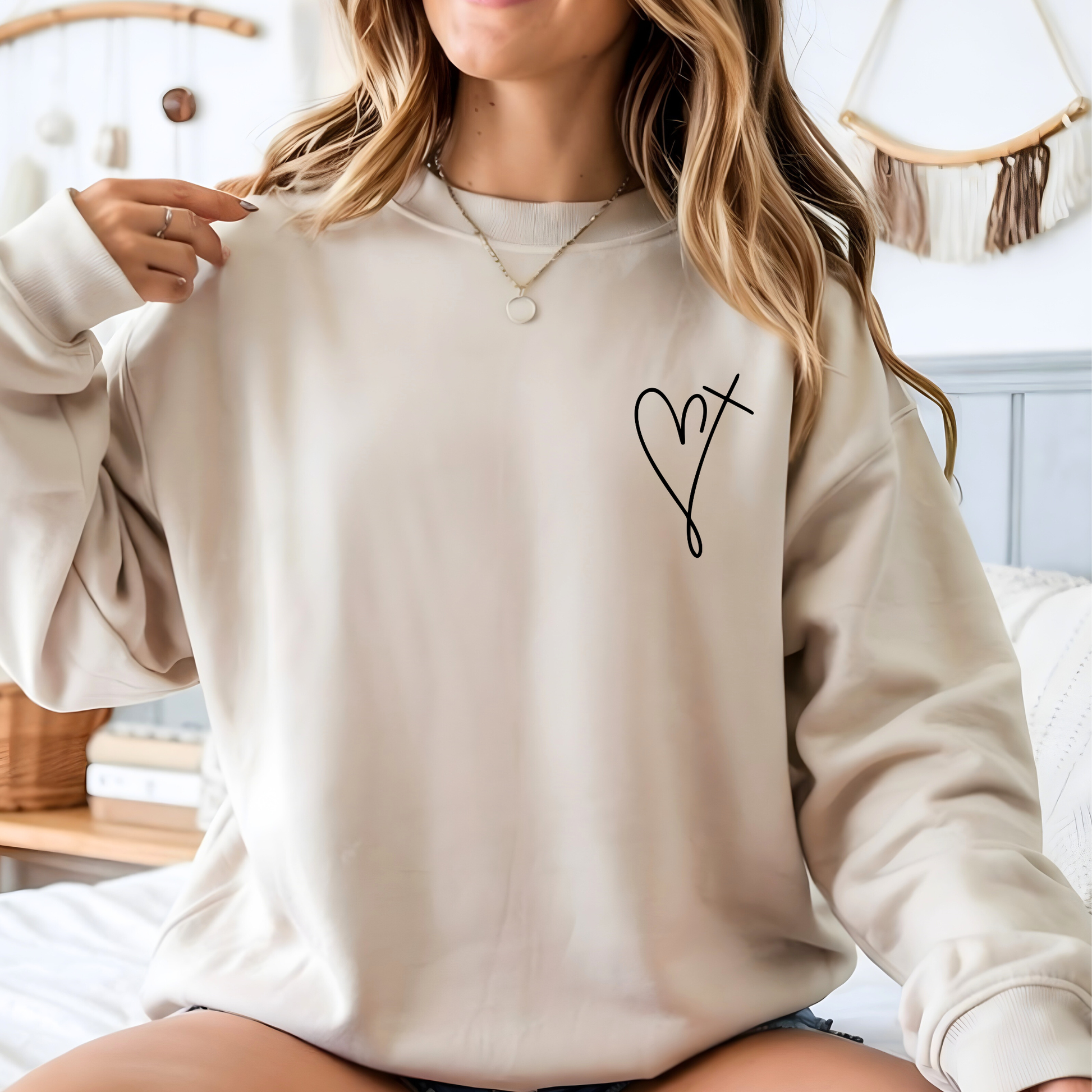 Person wearing a beige sweatshirt with a black heart design in a casual setting.