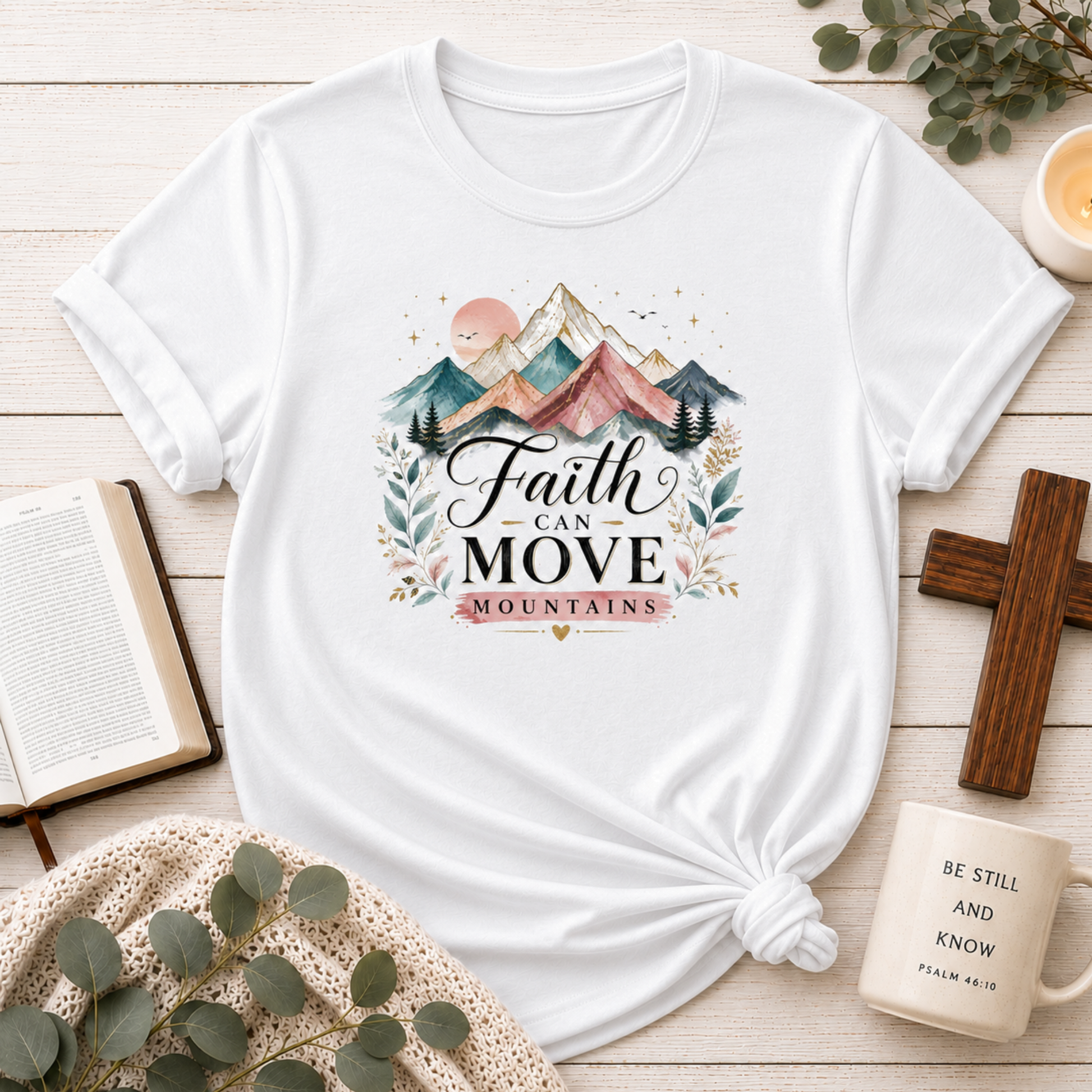 White t-shirt with 'Faith Can Move Mountains' design on a wooden surface with decor items.