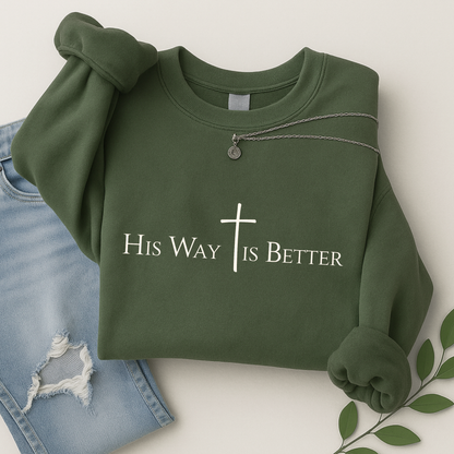 Green “His Way Is Better” Christian sweatshirt folded beside jeans and greenery