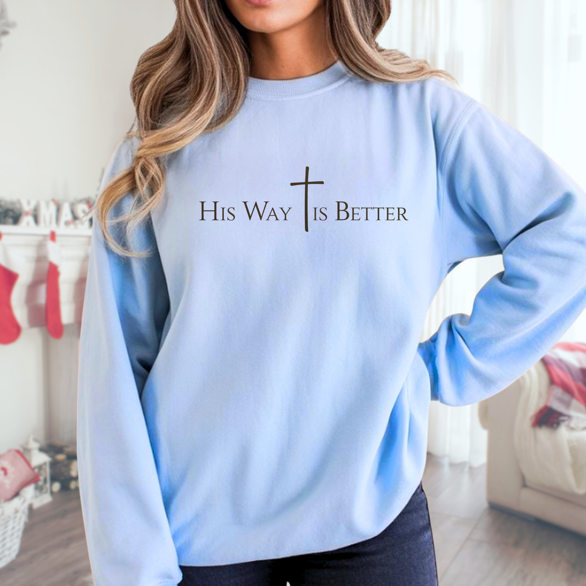 Woman wearing sky blue “His Way Is Better” sweatshirt standing in living room