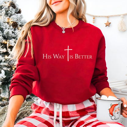 Woman wearing red “His Way Is Better” sweatshirt holding Santa mug near Christmas tree