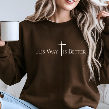 Woman wearing brown “His Way Is Better” cross sweatshirt holding mug