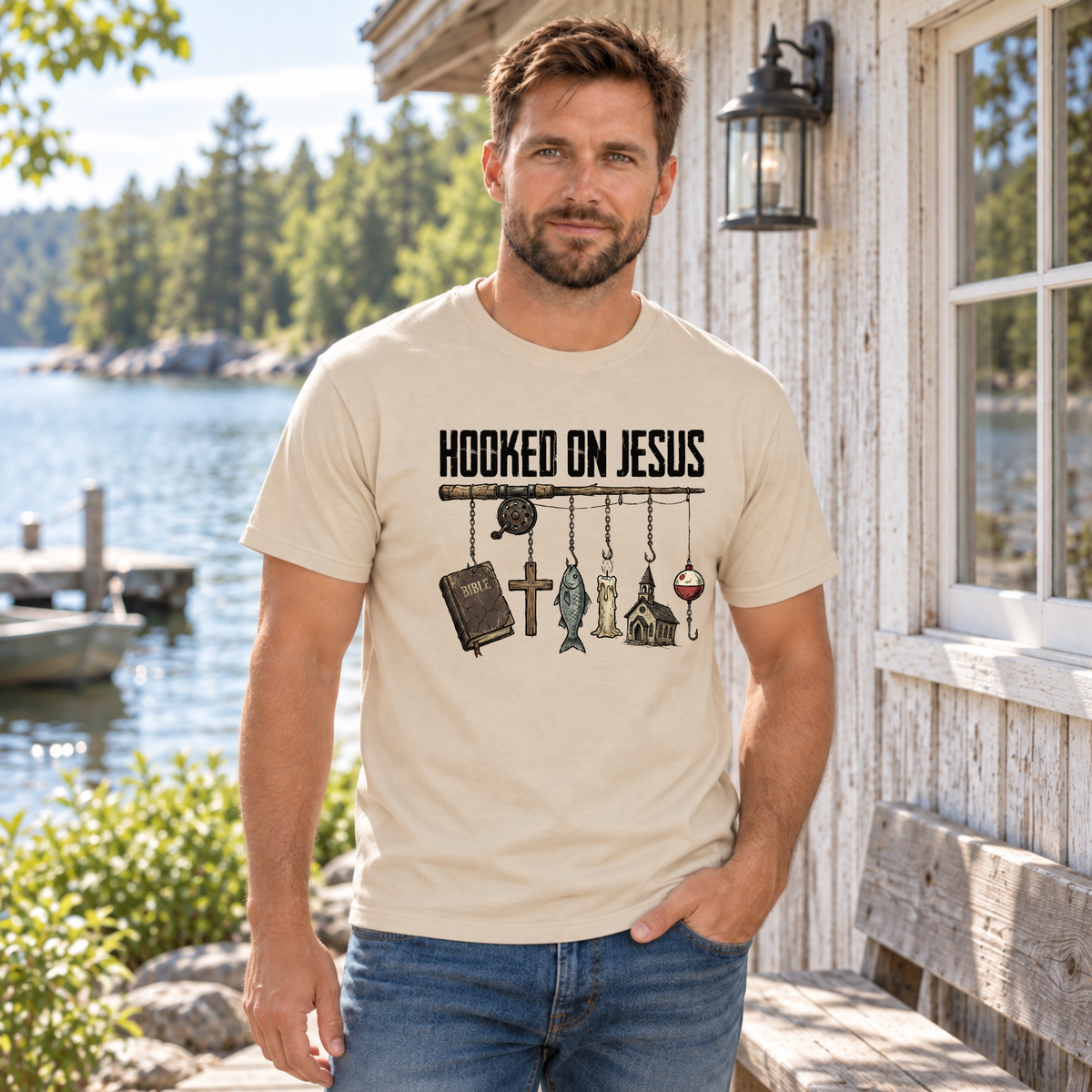 Man wearing a sand Hooked on Jesus T-shirt beside a lakeside cabin.