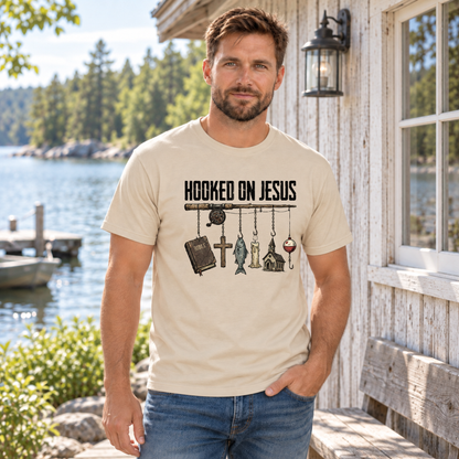 Man wearing a sand Hooked on Jesus T-shirt beside a lakeside cabin.