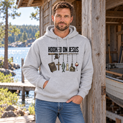 Man wearing a sports gray Hooked on Jesus hoodie beside a rustic boathouse.