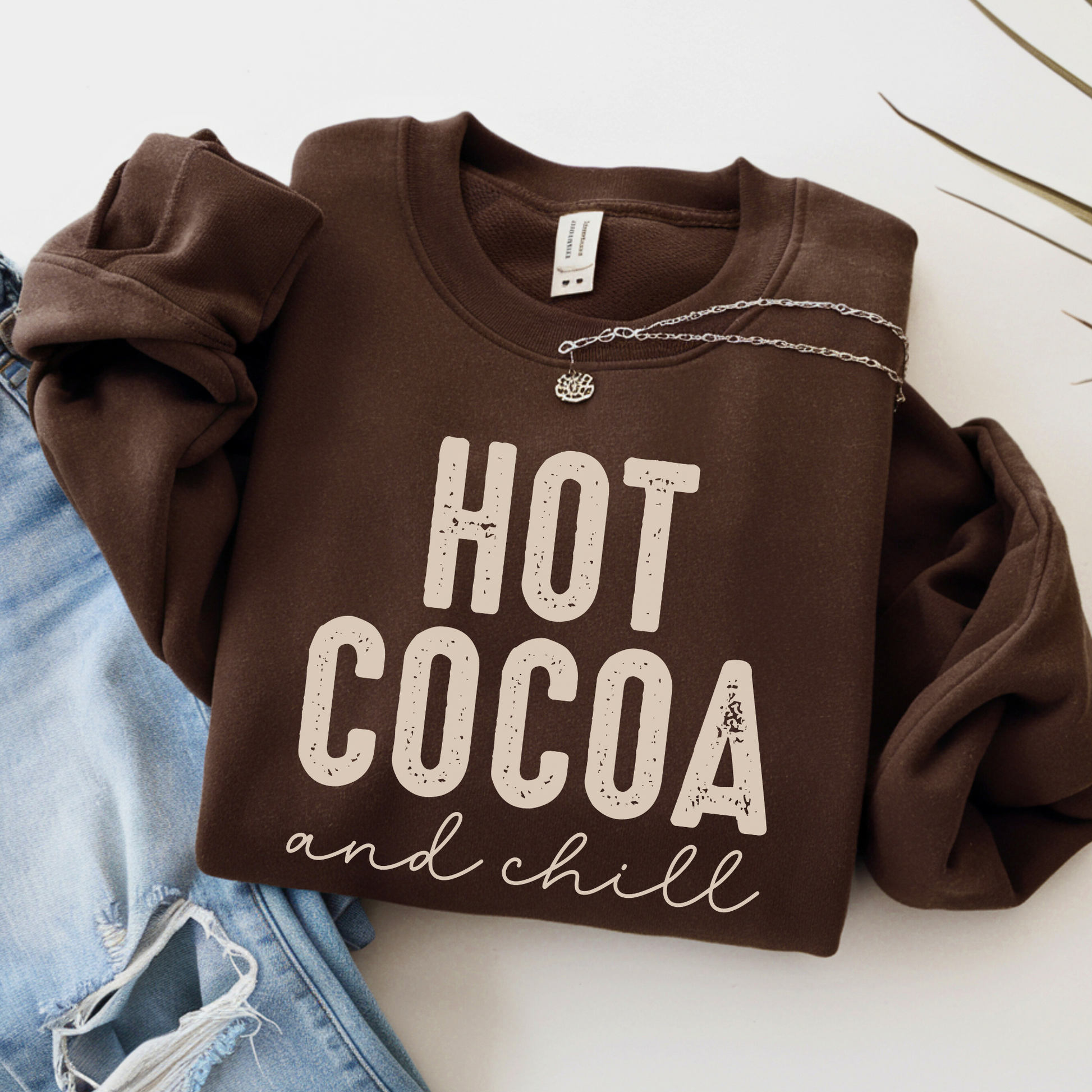 Hot Cocoa and Chill sweatshirt in brown – flat lay with necklace and ripped jeans
