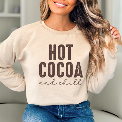 Woman wearing a beige sweatshirt with 'Hot Cocoa and Chill' text in a cozy indoor setting.