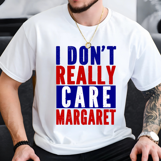 Man sitting and wearing a white patriotic graphic tee with red, white, and blue block lettering that says "I Don’t Really Care Margaret"