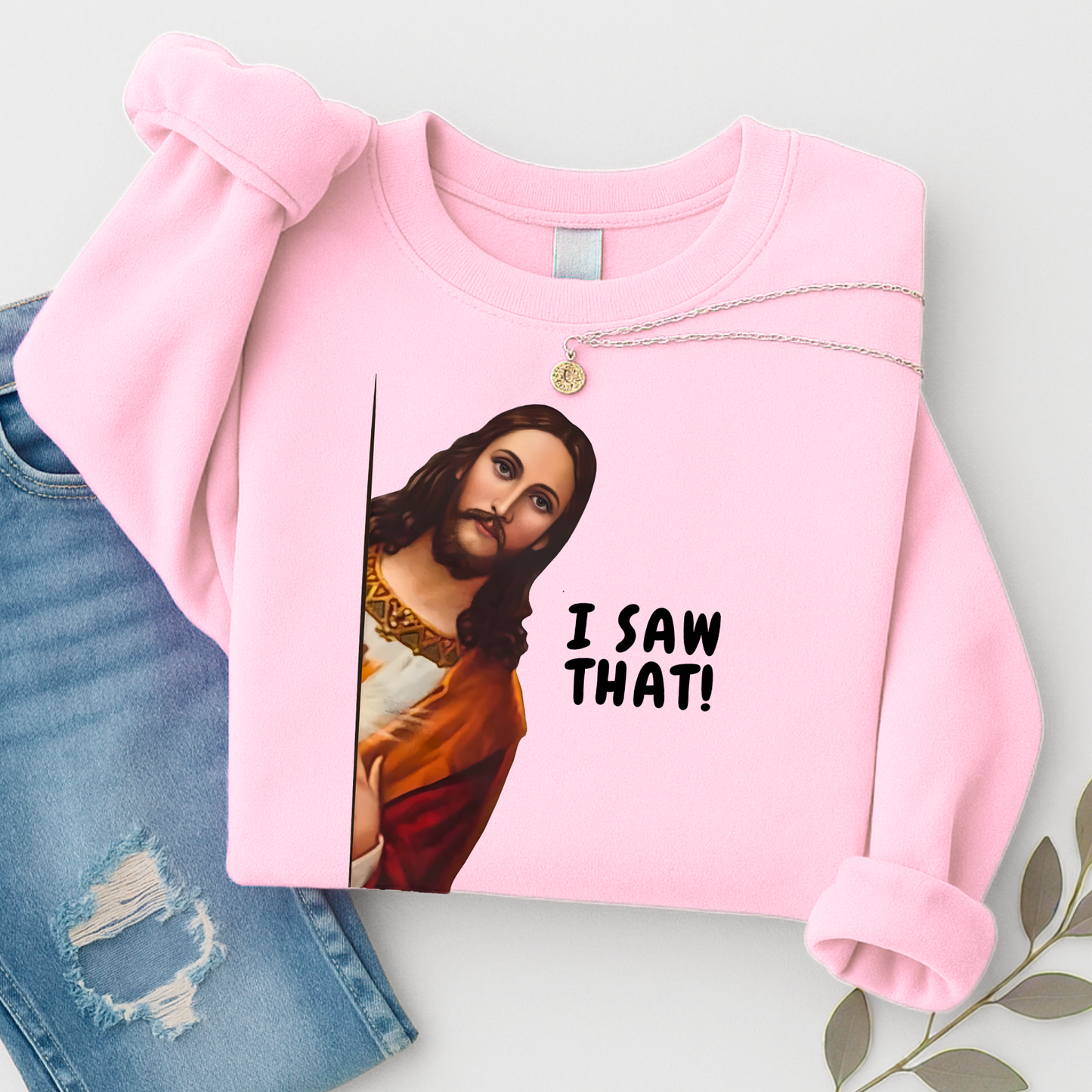 Pink sweatshirt with a graphic of a religious figure and 'I saw that!' text, paired with jeans on a light background.