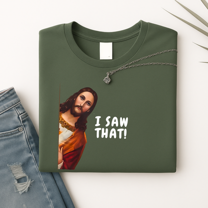 Green  flatlay Tshirrt  with a graphic of a Jesus saying 'I SAW THAT!' text, paired with jeans and leaves on a light background.