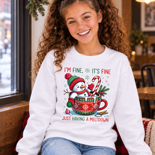 Girl seated by a snowy cafe window wearing a white youth sweatshirt with an I'm Fine It's Fine snowman meltdown design