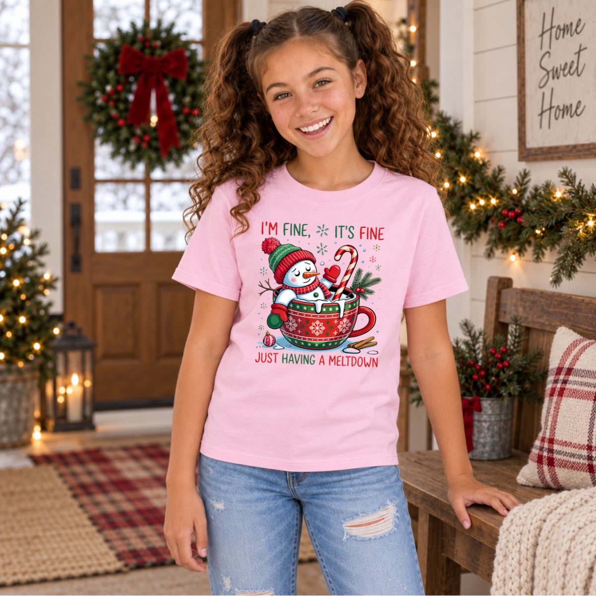 Girl wearing a light pink youth T-shirt with an I'm Fine It's Fine snowman meltdown Christmas design in a festive entryway