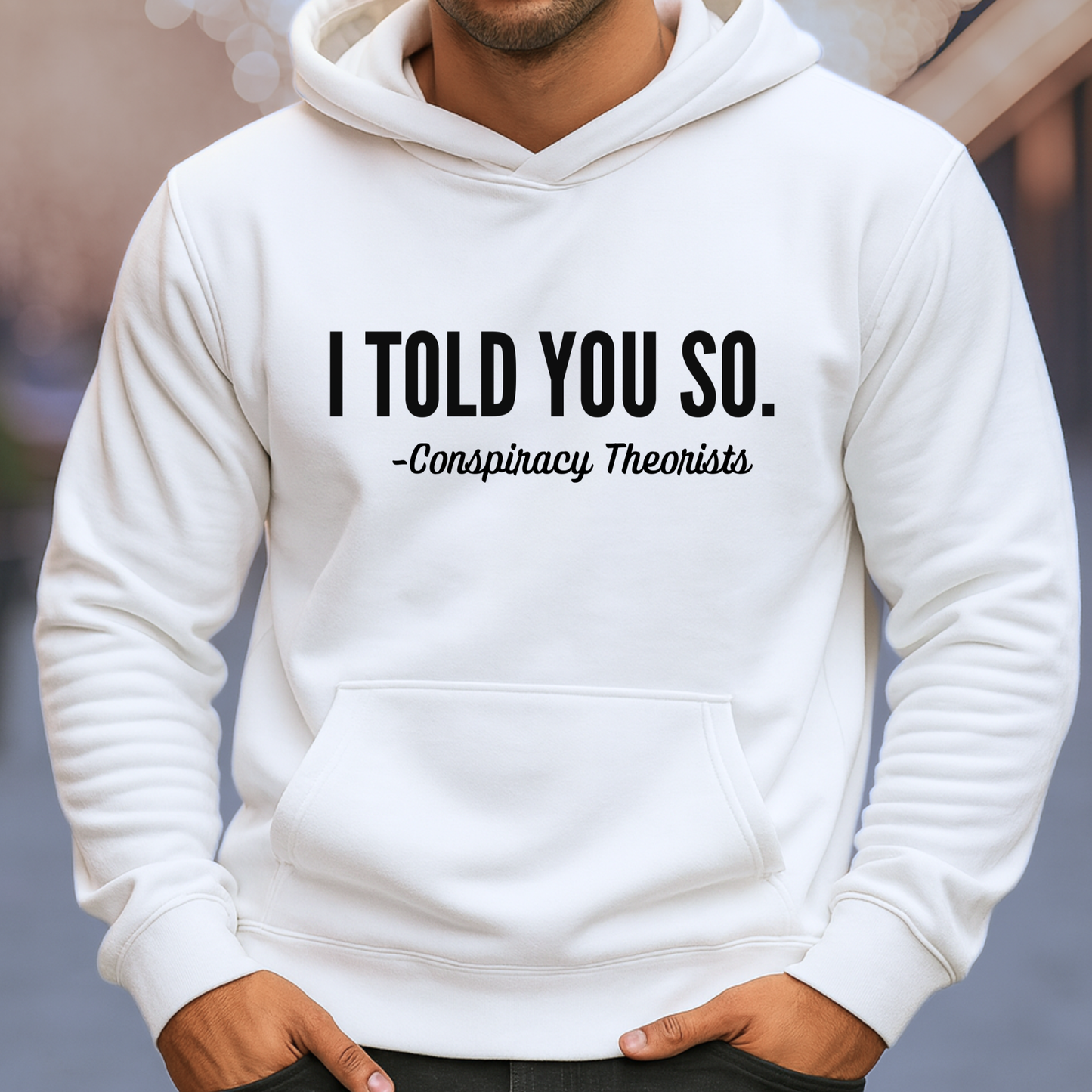 Man wearing white pullover hoodie with bold “I Told You So – Conspiracy Theorists” graphic