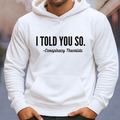 Man wearing white pullover hoodie with bold “I Told You So – Conspiracy Theorists” graphic
