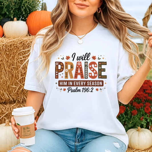 Woman wearing white “I Will Praise Him In Every Season” T-shirt at pumpkin patch holding coffee cup

