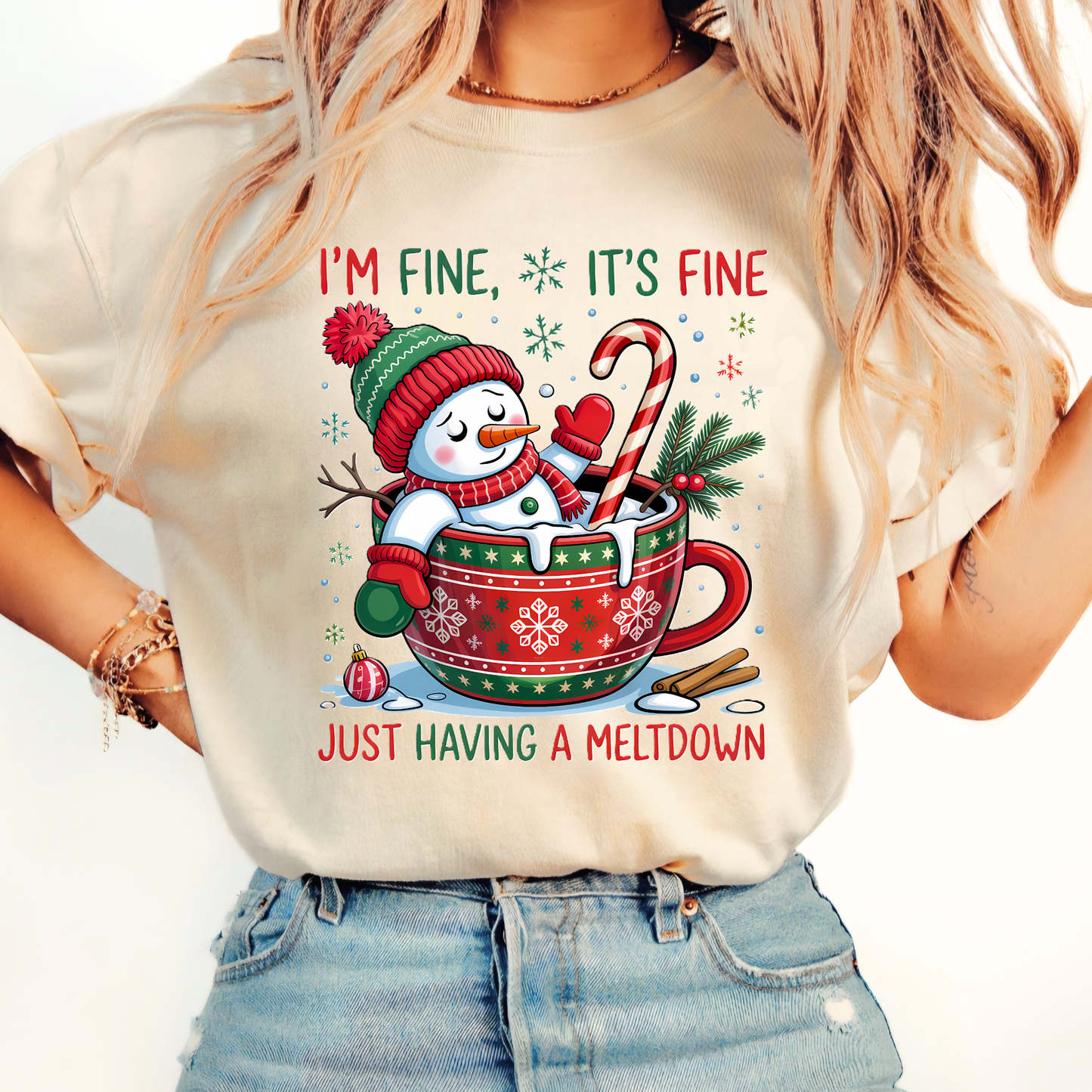 Woman wearing sand-colored Christmas shirt with snowman and cocoa mug graphic.
