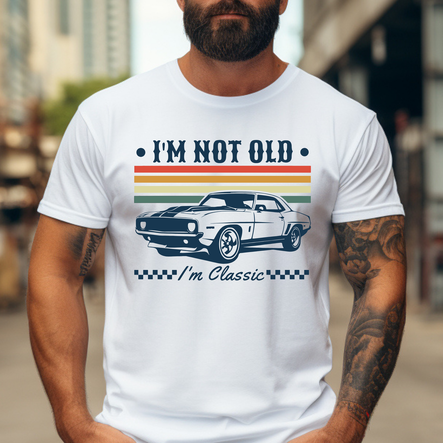 A bearded man wearing a white "I'm Not Old – I'm Classic" T-shirt with a retro muscle car design and vintage racing stripes in orange, yellow, and green. The graphic tee has a bold, nostalgic feel and is perfect for men who love cars and classic style. Great gift idea for car enthusiasts and birthdays.
