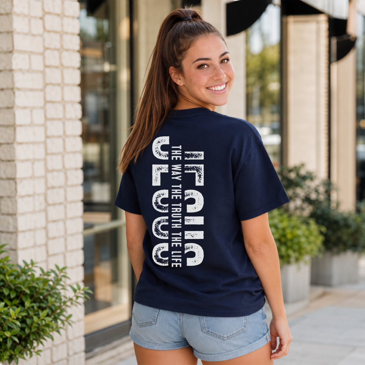 Woman shown from behind wearing a navy T-shirt with vertical white JESUS lettering and “The Way, The Truth, The Life” text.