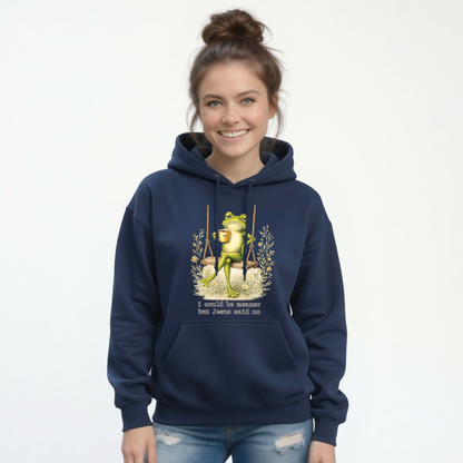 Woman modeling a navy hoodie with a frog sitting on a swing holding a mug and the words “I could be meaner but Jesus said no.”