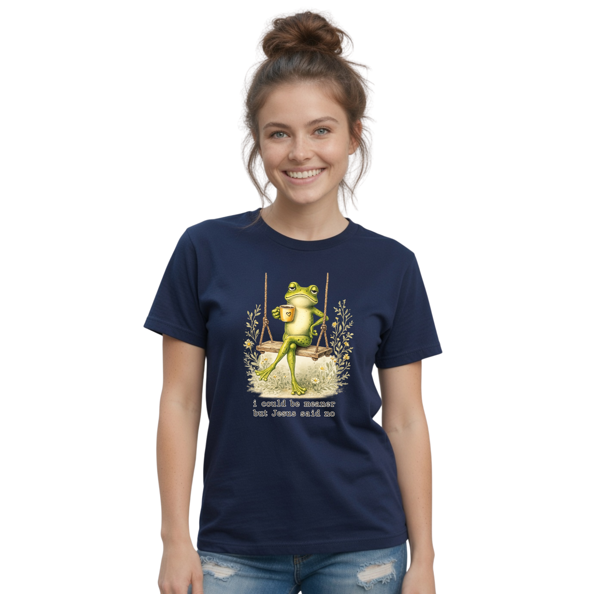 Woman modeling a navy T-shirt with a frog sitting on a swing holding a mug and the words “I could be meaner but Jesus said no.”