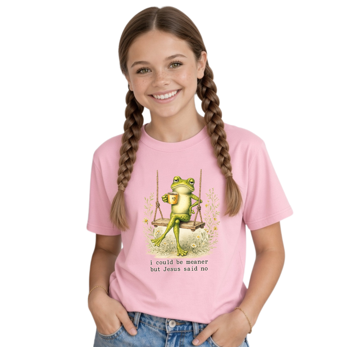 Youth girl wearing a light pink T-shirt with the I Could Be Meaner But Jesus Said No frog-on-a-swing faith design.