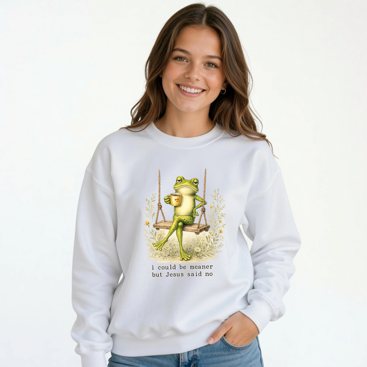 Young girl wearing a white crewneck sweatshirt with the I Could Be Meaner But Jesus Said No frog-on-a-swing Christian design.