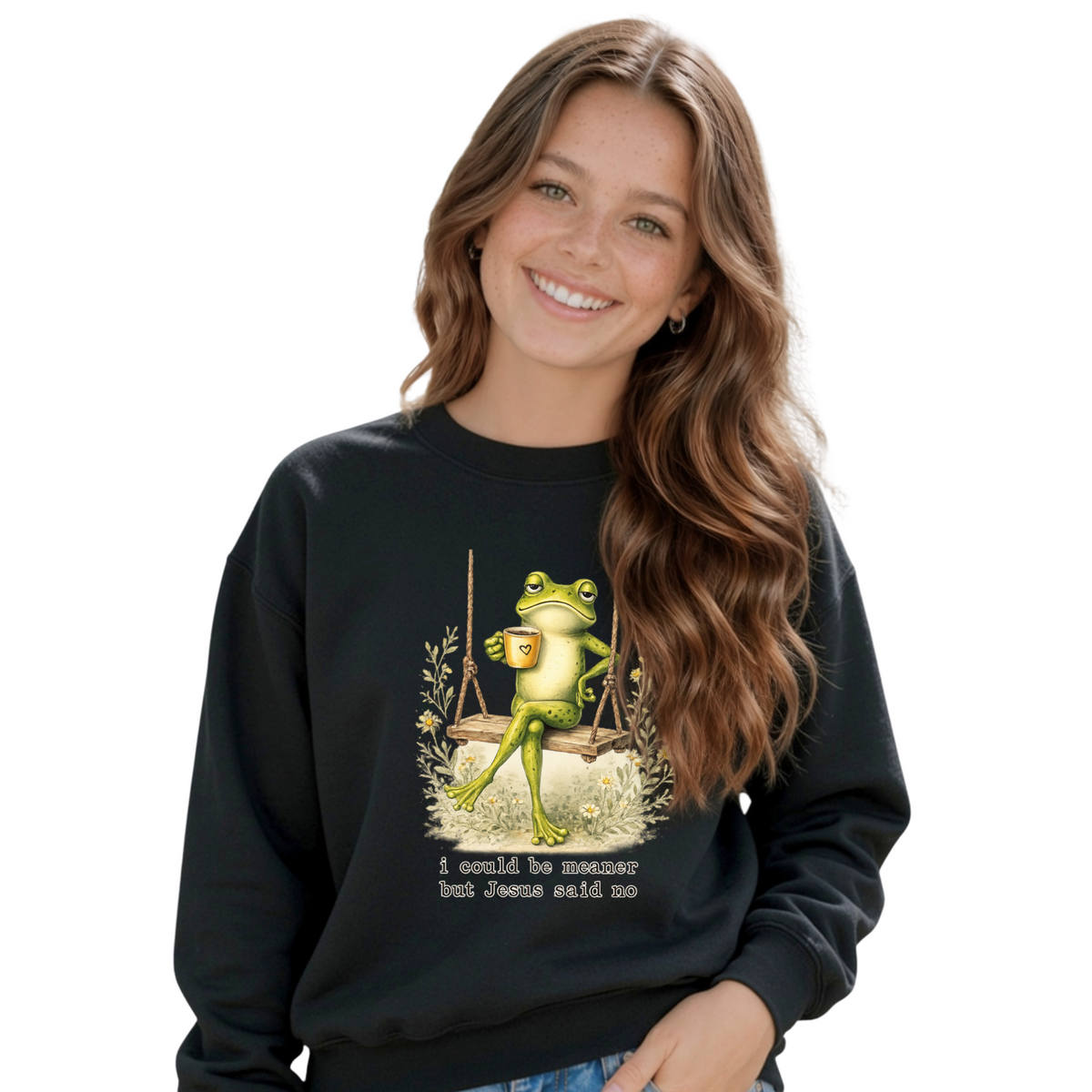 Young girl wearing a black crewneck sweatshirt with the I Could Be Meaner But Jesus Said No frog-on-a-swing Christian design.