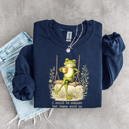 Folded navy crewneck sweatshirt flat lay with the I Could Be Meaner But Jesus Said No frog-on-a-swing faith design.