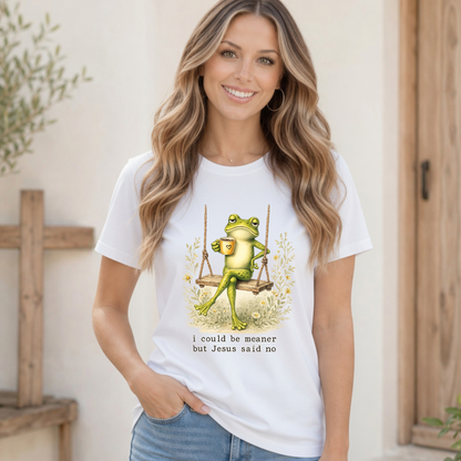 Woman modeling a white T-shirt with a frog sitting on a swing holding a mug and the words “I could be meaner but Jesus said no.”