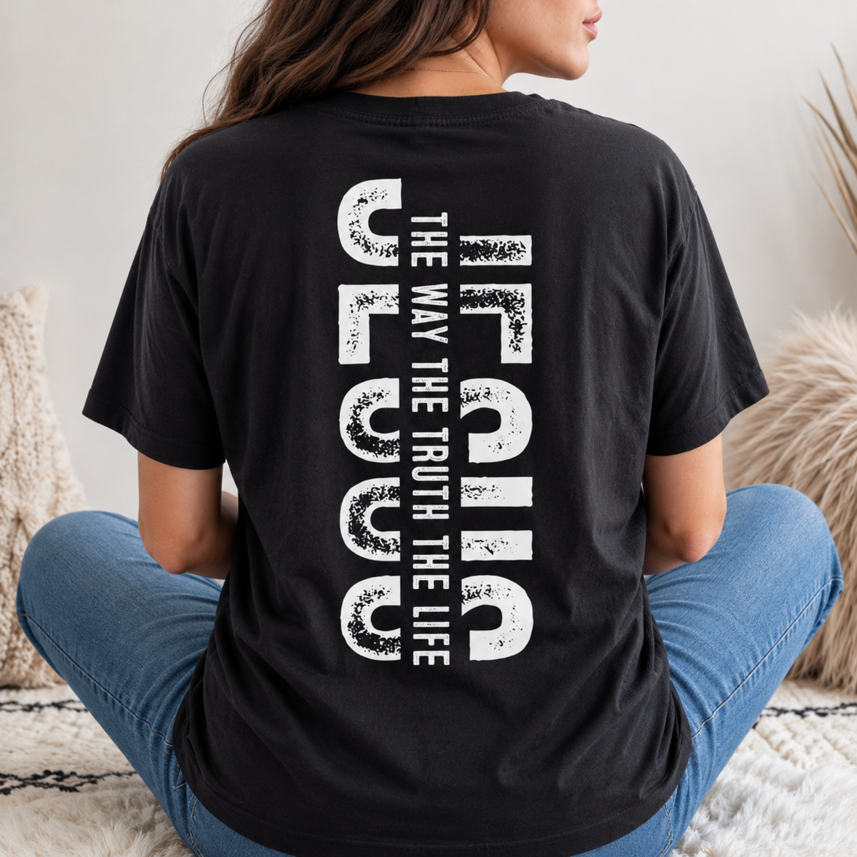 Woman shown from behind wearing a black T-shirt with vertical white JESUS lettering and “The Way, The Truth, The Life” text.