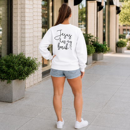 Back view of a woman wearing a white Jesus Has My Back crewneck sweatshirt with black script lettering and a heart cross graphic.
