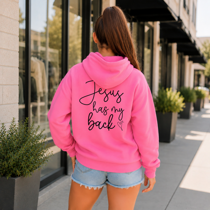 Back view of a woman wearing a Bright Pink Jesus Has My Back hoodie with black script lettering and a heart cross graphic.